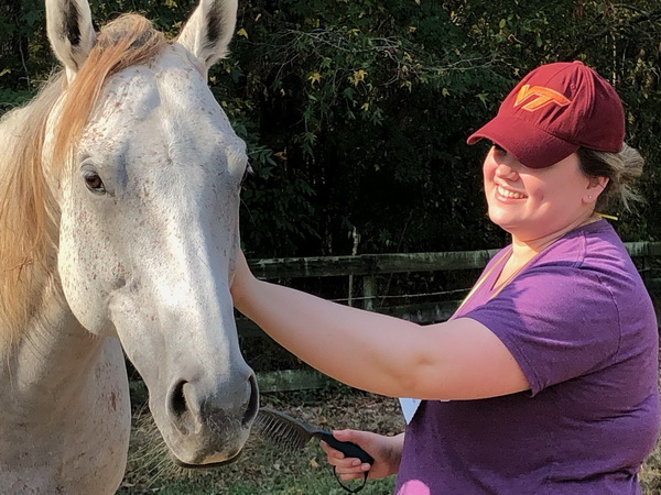 woman with a red Virginia Tech hat smiling while petting a white horse