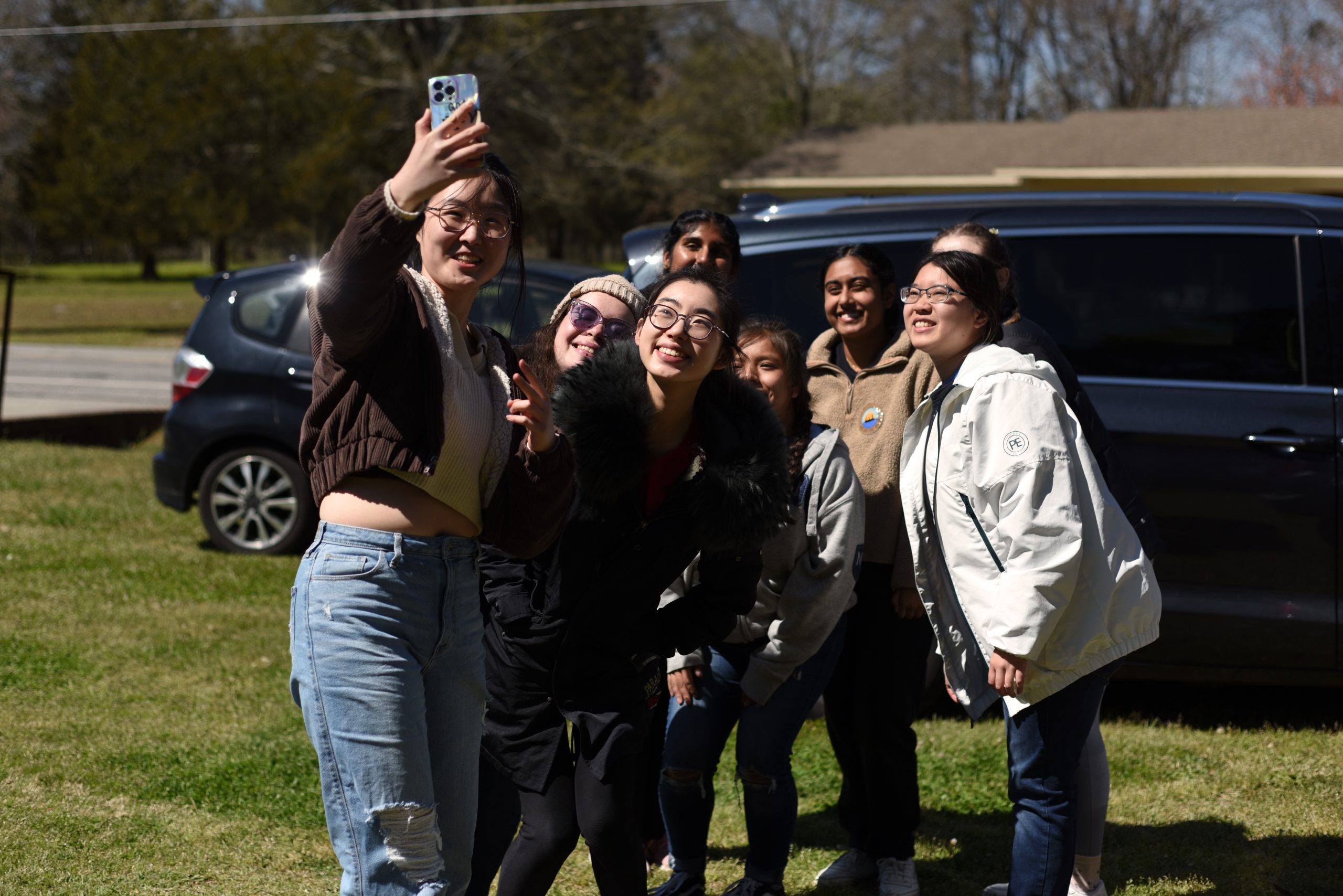 A group of college students posed in front of a van taking a selfie photo.