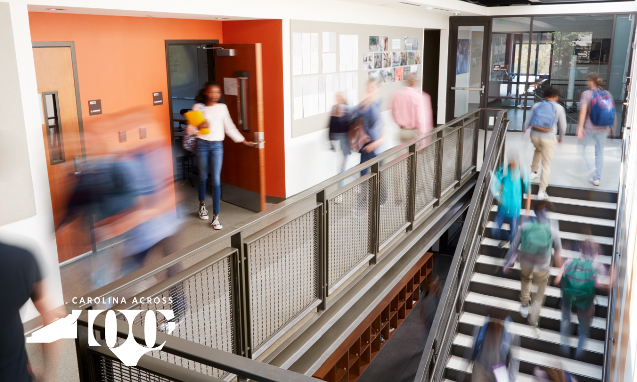 Student coming out of a classroom while other students walk down a hallway toward the stairs.